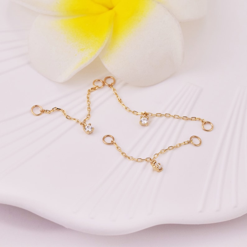 May include: Three gold chains with small clear gemstones hanging from each end. The chains are on a white surface.