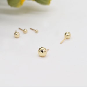 Pu&ograve; includere: Tre paia di orecchini a lobo con sfera d'oro. Gli orecchini sono piccoli e semplici, con una forma sferica.