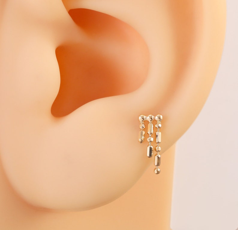 May include: Gold dangle earring with a chain of small round and rectangular beads.