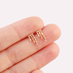 May include: A pair of gold dangle earrings with a chain of small round and rectangular beads.