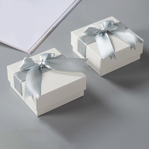 May include: Two white gift boxes with silver ribbon bows. The boxes are on a gray surface.