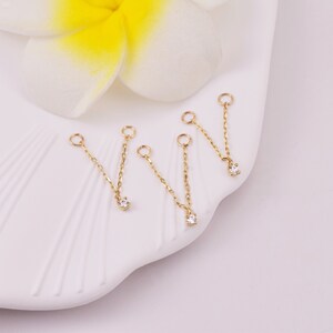 May include: Four gold chain connectors with a small clear rhinestone at the end of each chain. The chains are on a white surface.