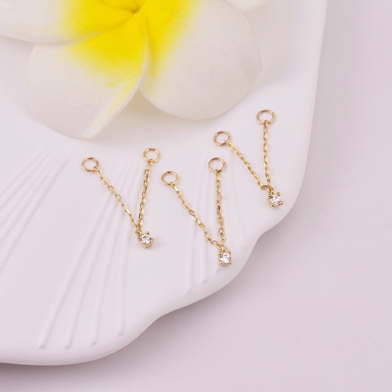 May include: Four gold chain connectors with a small clear rhinestone at the end of each chain. The chains are on a white surface.
