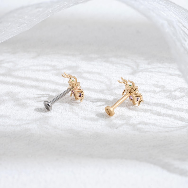 May include: Two gold scorpion body jewelry pieces with clear and purple gemstones. The jewelry is on a white surface.