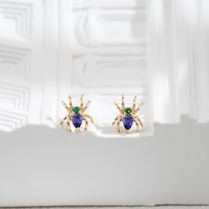 May include: A pair of gold spider earrings with purple and green gemstones.