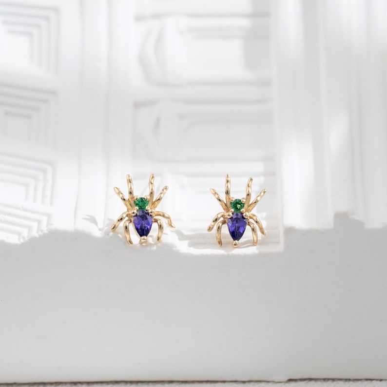 May include: A pair of gold spider earrings with purple and green gemstones.