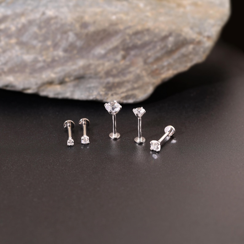 Pu&ograve; includere: Quattro pezzi di gioielleria per il corpo in argento con pietre di zircone cubico trasparenti. I gioielli sono disposti su una superficie nera.