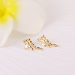 May include: A pair of gold dangle earrings with a geometric design. The earrings are made of small, round beads and rectangular shapes.