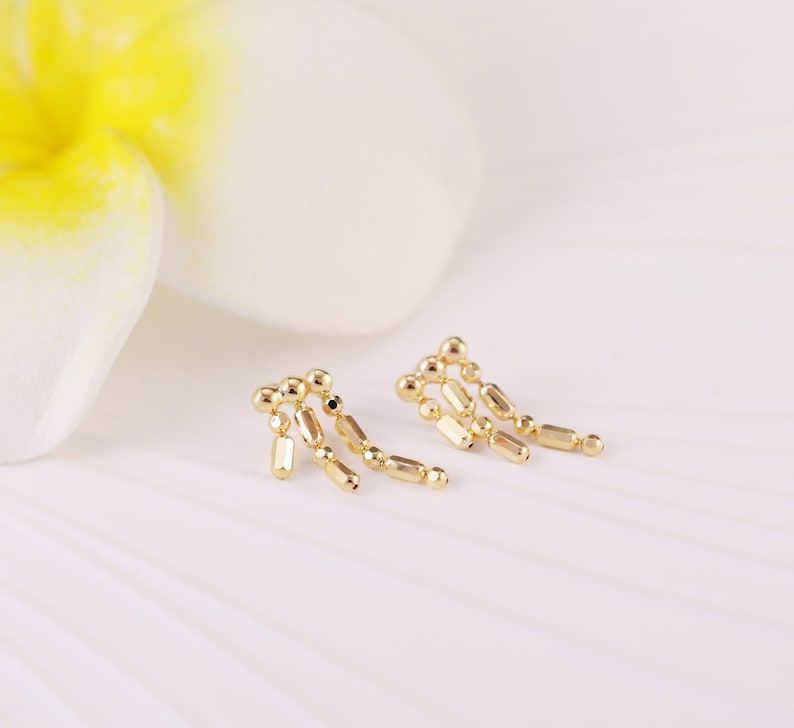 May include: A pair of gold dangle earrings with a geometric design. The earrings are made of small, round beads and rectangular shapes.