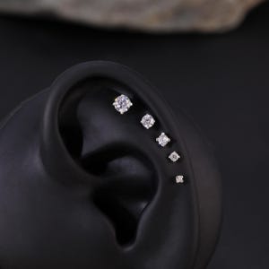 Pu&ograve; includere: Primo piano di un modello di orecchio nero con cinque piccole pietre preziose rotonde e trasparenti incastonate in argento.