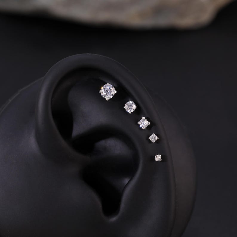 Pu&ograve; includere: Primo piano di un modello di orecchio nero con cinque piccole pietre preziose rotonde e trasparenti incastonate in argento.