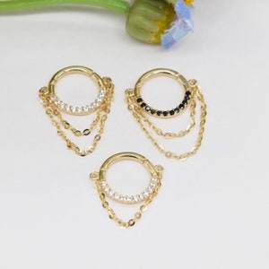 May include: Three gold hoop earrings with dangling chains. The hoops are adorned with small clear or black gemstones.