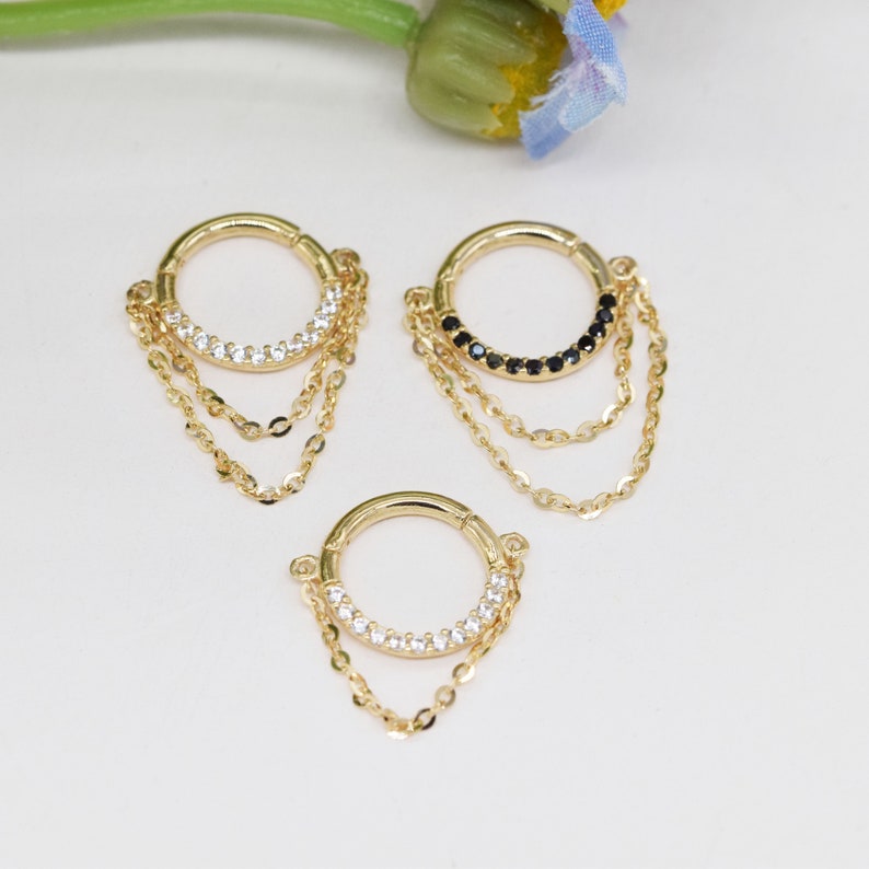 May include: Three gold hoop earrings with dangling chains. The hoops are adorned with small clear or black gemstones.