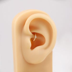 May include: A gold-colored hoop earring with a small, clear gemstone. The earring is set in a model ear, showcasing the jewelry's design and placement. The earring is a simple, elegant piece.