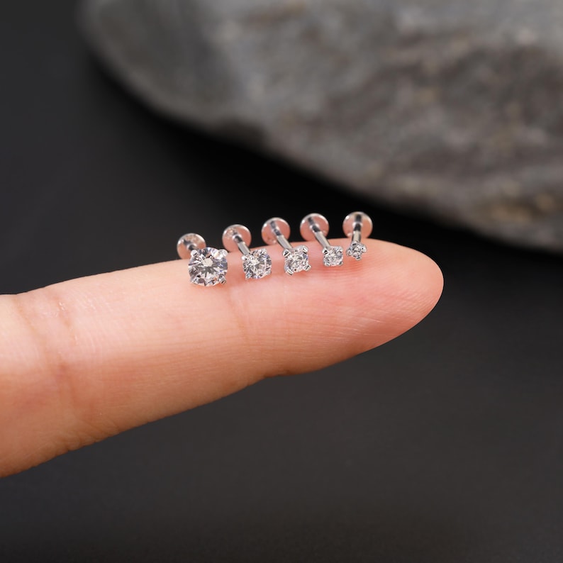 Pu&ograve; includere: Cinque perni per il naso argentati con pietre di zircone cubico trasparenti di diverse dimensioni. I perni sono allineati su un dito, con la pietra pi&ugrave; grande a sinistra e la pi&ugrave; piccola a destra.