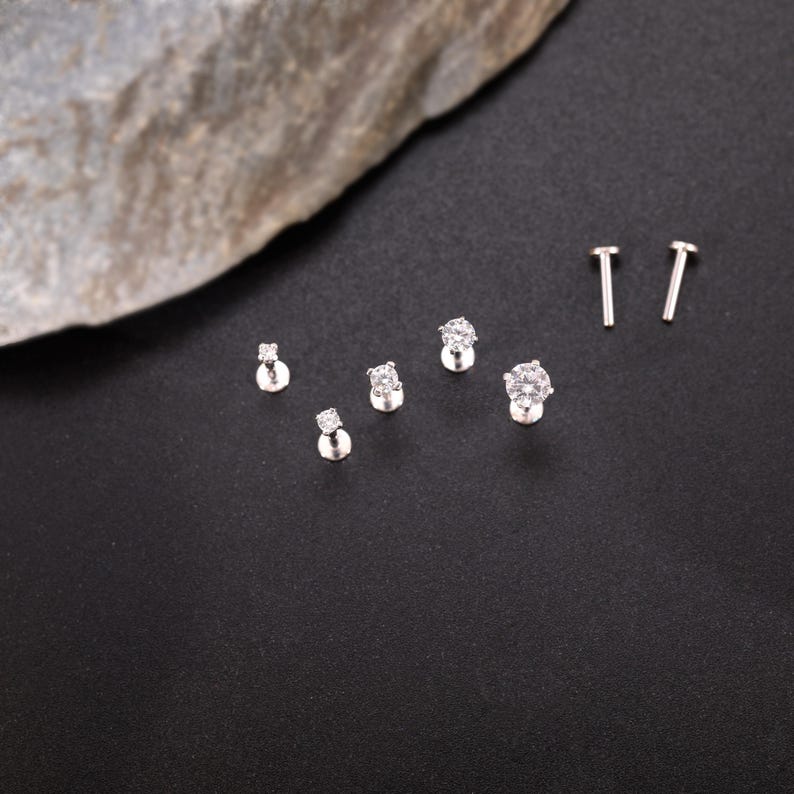 Pu&ograve; includere: Un set di sei orecchini a perno in argento con pietre di zircone cubico trasparenti. Gli orecchini sono disposti in fila su una superficie nera. Gli orecchini sono di diverse dimensioni, con l'orecchino pi&ugrave; grande al centro.
