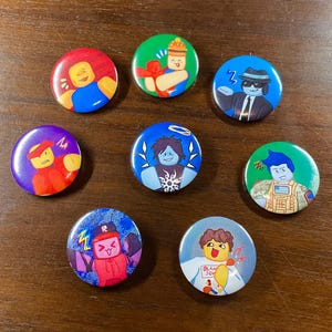 May include: A collection of eight colorful round buttons with cartoon character designs. The buttons feature various characters in different poses and outfits, set against backgrounds of blue, green, red, and purple.