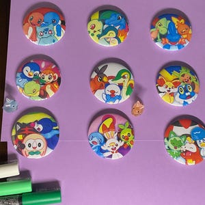 May include: Nine round, colorful buttons featuring different Pokemon characters. The buttons are all approximately 2 inches in diameter and have a white background.