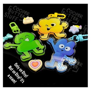 May include: Three acrylic character keychains in green, yellow, and blue, each with a matching plastic clasp. The set includes small charms shaped like a heart, a star, and a round figure. Text on the image reads: Only on Etsy! Not on Etsy? It's a scam!