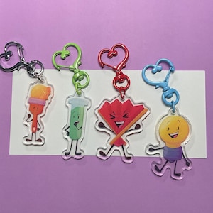 May include: Four colorful cartoon character keychains with heart-shaped metal clasps. The characters are a paintbrush, a test tube, a red fan, and a lightbulb. Each keychain is made of clear acrylic.