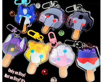 May include: Seven acrylic keychains shaped like ice lollies with various character designs, each featuring a metal lobster clasp. The designs include blue, purple, yellow, and pink colour schemes with wooden-style sticks. Text reads: Only on Etsy! Not on Etsy? It's a scam!