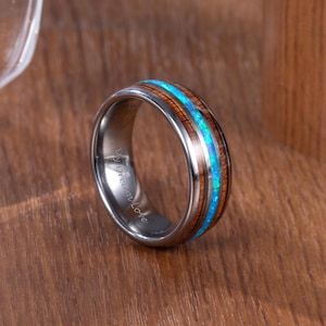 以下が含まれることがあります： 木材の象嵌と鮮やかな青色のオパールが中央にあるシルバーリング。リングの内側には「My Dream Love」の文字が刻まれています。リングは木製の表面に展示されています。