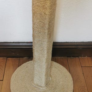 May include: A beige cat scratching post with a round base and a square top. The post is covered in natural sisal rope.