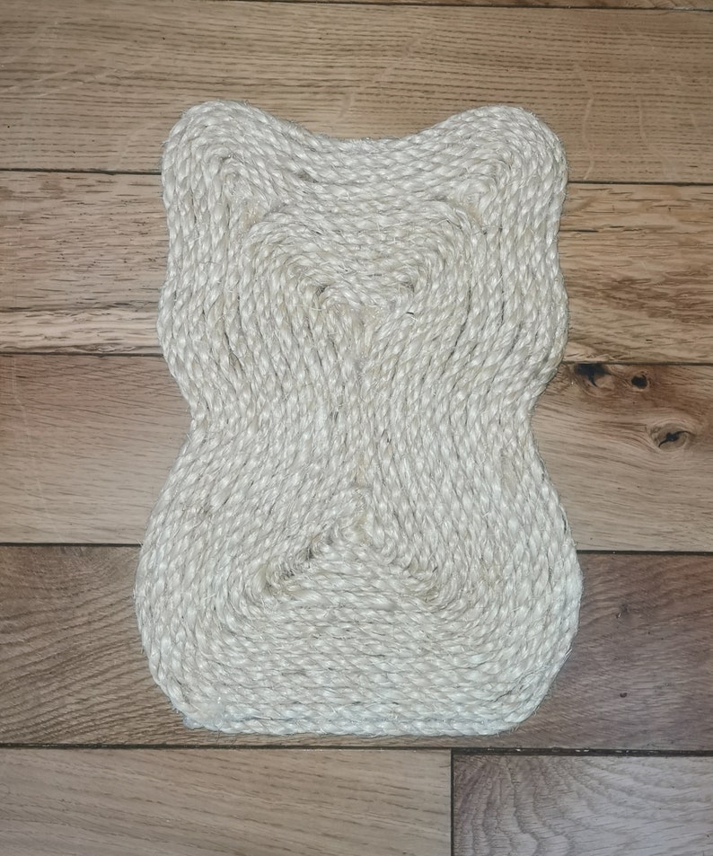 K&ouml;nnte beinhalten: Ein wei&szlig;er, geflochtener Seil-Teppich mit einer einzigartigen, organischen Form. Der Teppich ist aus Naturfasern gefertigt und hat eine strukturierte Oberfl&auml;che.