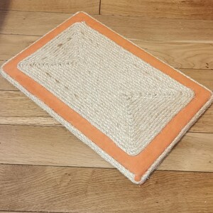 Puede incluir: Un rascador rectangular para gatos con una superficie de cuerda de sisal natural y un borde naranja.