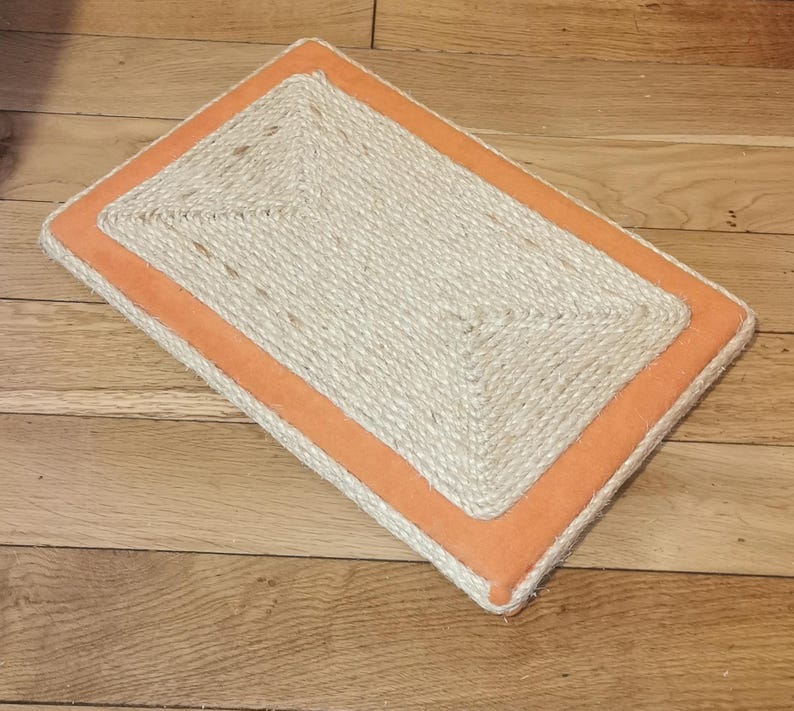 Puede incluir: Un rascador rectangular para gatos con una superficie de cuerda de sisal natural y un borde naranja.