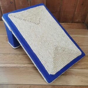 May include: A blue and beige cat scratching post with a sisal rope surface. The post is angled and has a blue fabric border.