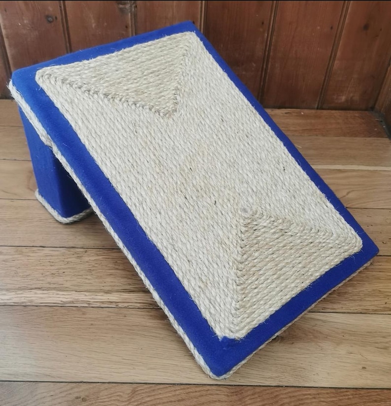 May include: A blue and beige cat scratching post with a sisal rope surface. The post is angled and has a blue fabric border.