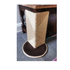 May include: A close-up of a brown and beige cat scratching post with a round base. The post is covered in sisal rope and has a brown fabric base.
