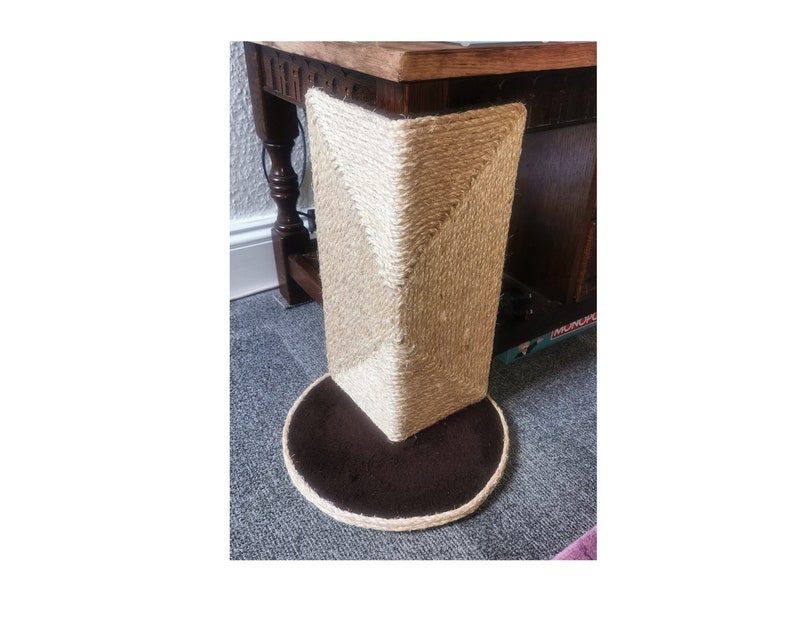 May include: A close-up of a brown and beige cat scratching post with a round base. The post is covered in sisal rope and has a brown fabric base.