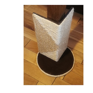 May include: A beige and white sisal-wrapped corner cat scratching post with a black circular base. The post is designed to be attached to a corner of a room.