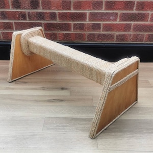 May include: A wooden cat scratching post with a natural rope covered scratching surface. The post is triangular in shape and has a light brown wood finish.