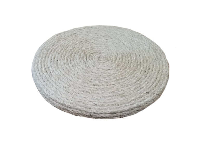 May include: A round, white, woven cushion made of natural fibers. The cushion is thick and has a circular pattern.