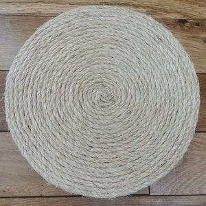 May include: A round, beige, woven coaster made of natural fibers. The coaster has a spiral pattern.