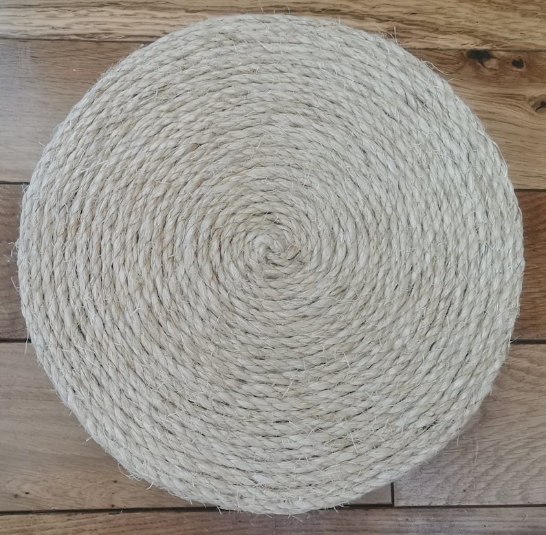 May include: A round, beige, woven coaster made of natural fibers. The coaster has a spiral pattern.