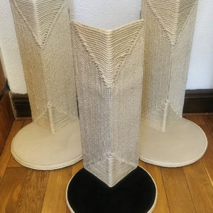May include: Three beige cat scratching posts with a rope-covered surface. The posts have a triangular shape and a round base. The base of the center post is black.