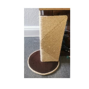 May include: A brown and beige cat scratching post with a round base. The post is covered in sisal rope and the base is covered in brown fabric.