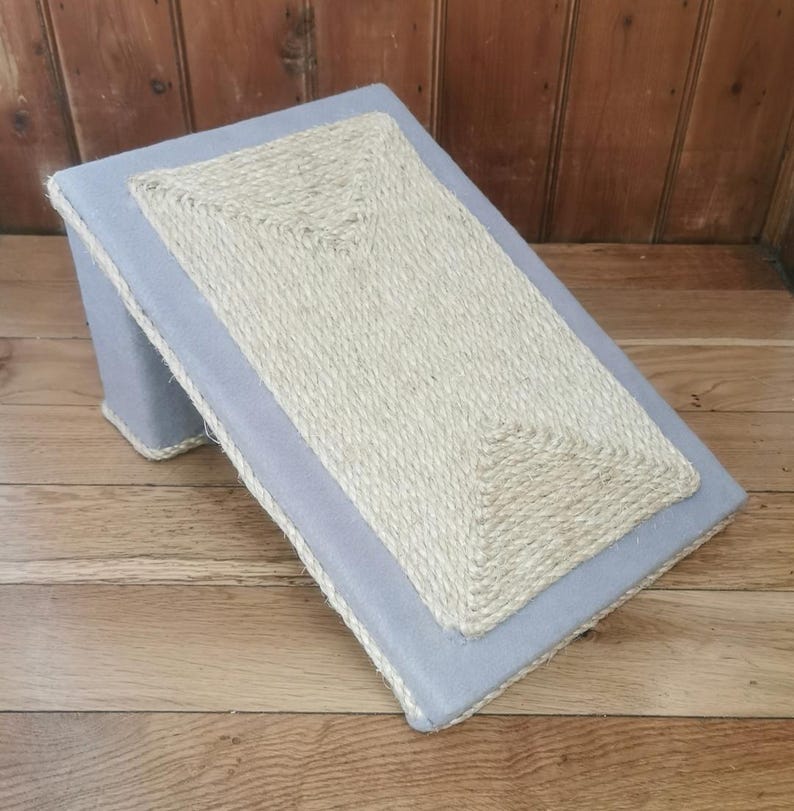 May include: A gray cat scratching post with a sisal rope surface. The post is angled and has a gray fabric border.