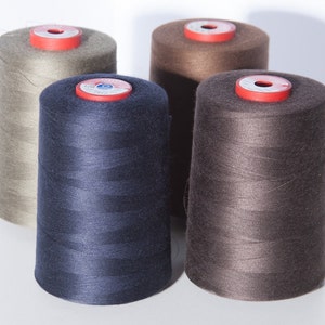 Puede incluir: Cuatro carretes de hilo de diferentes colores: beige, azul oscuro, marrón y marrón claro. Los carretes están dispuestos en semicírculo sobre una superficie blanca.