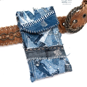 Könnte beinhalten: Ein brauner Ledergürtel mit geflochtenem Design und einem Handy-Etui aus Jeans. Das Handy-Etui besteht aus Patchwork-Jeans mit ausgefransten Kanten und weißen Nähten. Die Gürtelschnalle ist eine große, silberfarbene Metallschnalle mit einem dekorativen Design.