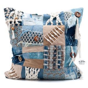 Könnte beinhalten: Ein Patchwork-Kissen mit verschiedenen blauen Jeansstoffen, beigem Cord und weißen Makramee-Akzenten. Das Kissen hat Holzknöpfe und dekorative Quasten. Das Design kombiniert verschiedene Texturen und Muster.
