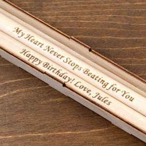 Peut inclure: Deux crayons en bois dans une bo&icirc;te en bois. Les crayons sont grav&eacute;s avec le message "My Heart Never Stops Beating for You Happy Birthday! Love, Jules".