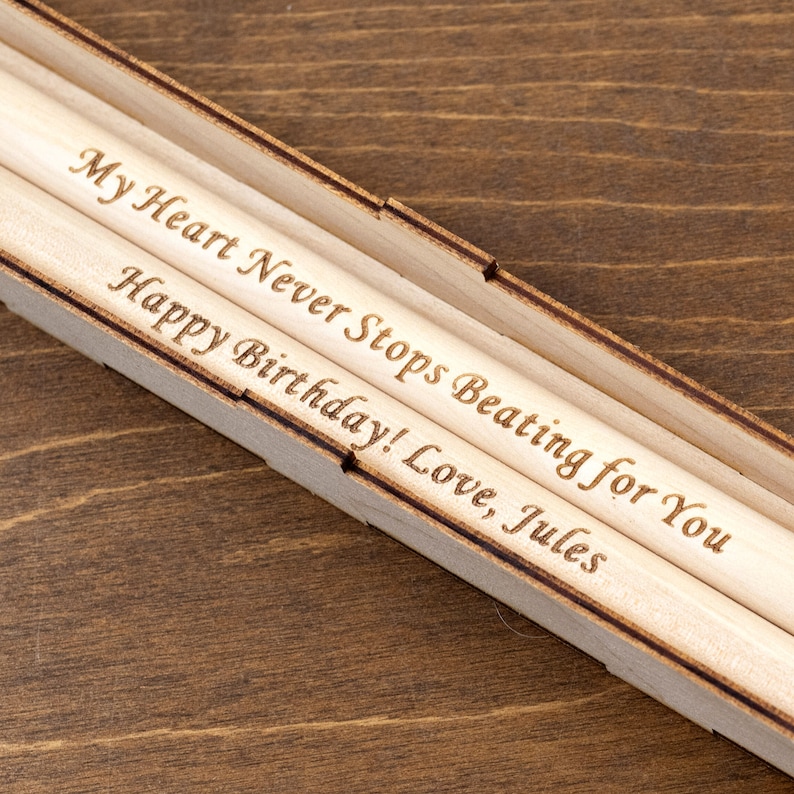 Peut inclure: Deux crayons en bois dans une bo&icirc;te en bois. Les crayons sont grav&eacute;s avec le message "My Heart Never Stops Beating for You Happy Birthday! Love, Jules".
