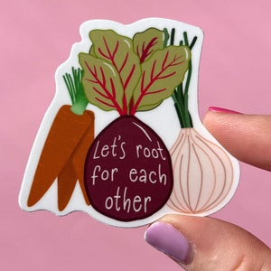 Könnte beinhalten: Ein weißer Aufkleber mit einer Cartoon-Illustration einer Rübe, einer Karotte und einer Zwiebel. Die Rübe hat den Text "Let's root for each other" darauf geschrieben.
