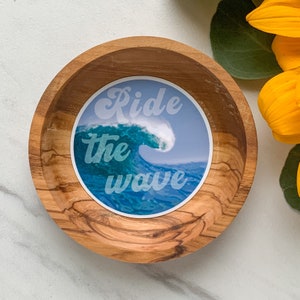 May include: A wooden bowl with a blue and white sticker that says "Ride the wave". The sticker features a stylised wave with a white crest.
