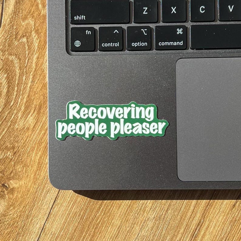 May include: A green sticker with white text that reads "Recovering people pleaser" on a silver laptop.